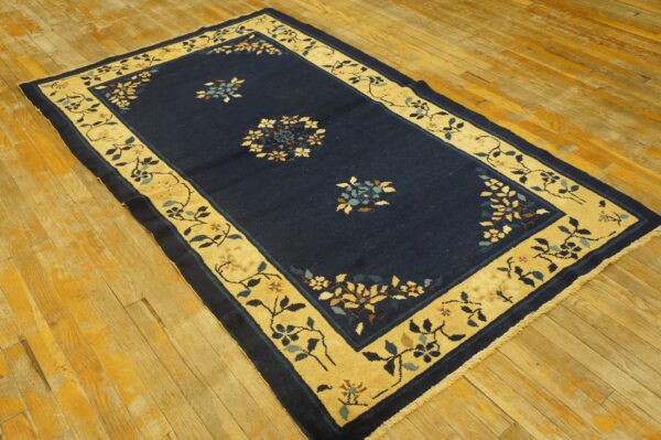 Navy blue rug with a gold floral border rests on a distressed golden hardwood floor.