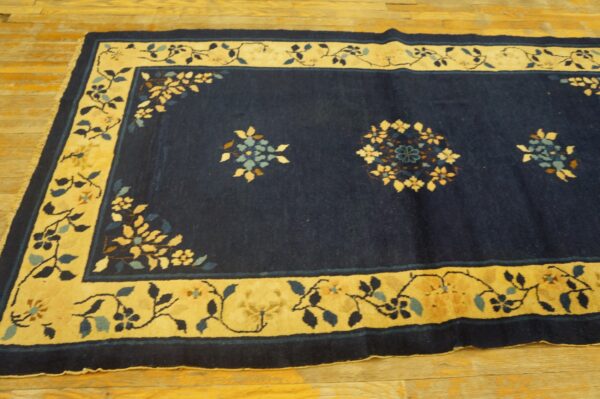 Navy blue rug with scattered floral medallions and a wide gold border rests on light wooden floors.