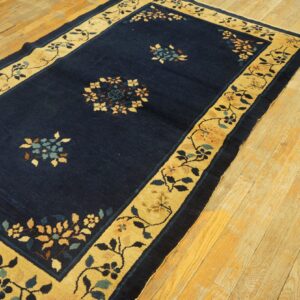 Dark blue rug with a wide tan floral border and scattered medallions on distressed wood flooring.