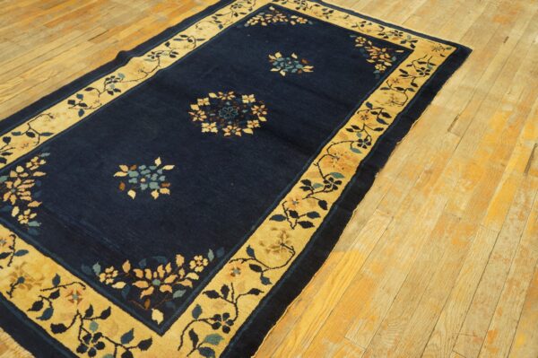 Dark blue rug with a wide tan floral border and scattered medallions on distressed wood flooring.