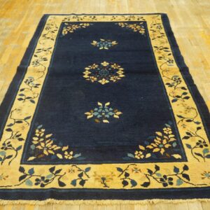 Dark blue rug with a golden floral border and central motifs lies on a distressed wooden plank floor.