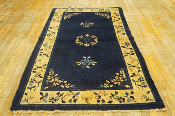 Dark blue rug with a golden floral border and central motifs lies on a distressed wooden plank floor.