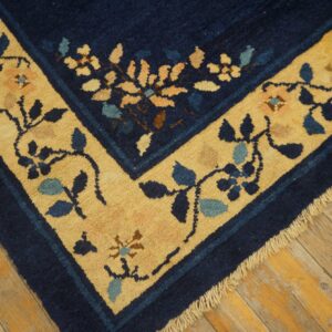 Close-up of a navy blue rug corner showing a golden yellow border with intricate blue and pink floral patterns on wood flooring.