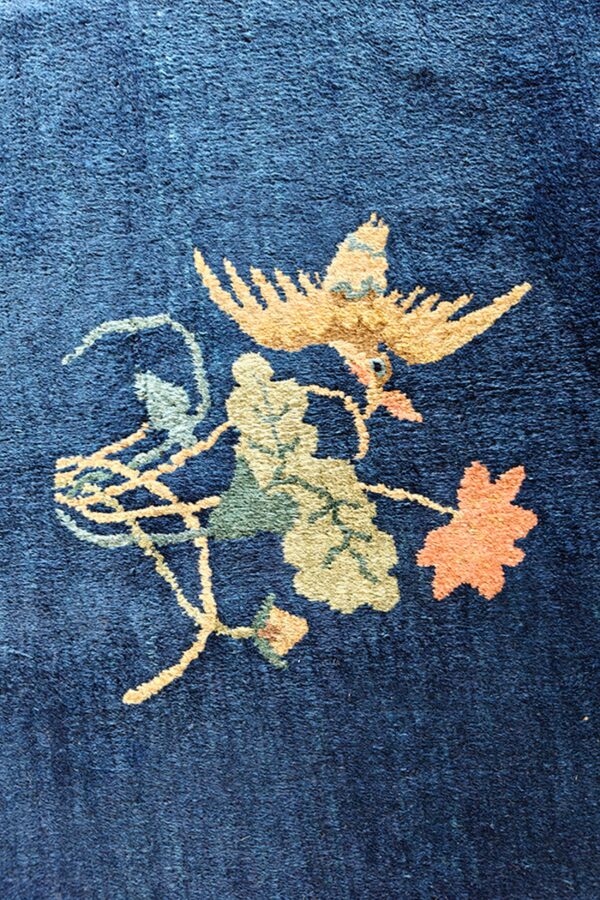 Detailed view of a deep blue rug with a yellow bird and orange and green floral design.