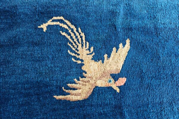 A close-up shows the textured, deep blue pile and a central beige flying bird motif.