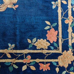 Plush blue rug corner featuring a beige bamboo border, coral flowers, and a tan bird motif.