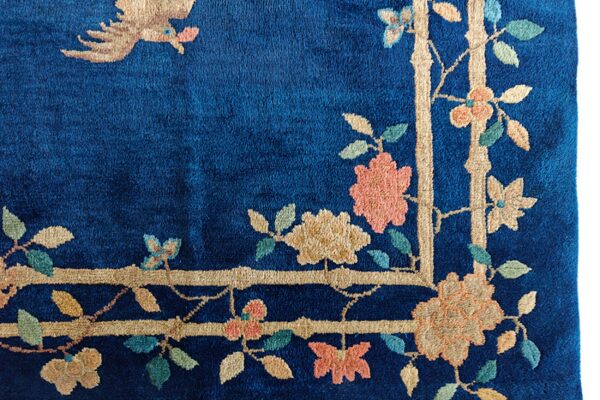 Plush blue rug corner featuring a beige bamboo border, coral flowers, and a tan bird motif.