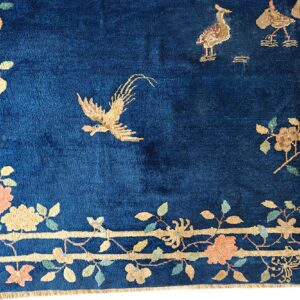 Blue rug detail with golden birds and a border pattern of bamboo stalks, pink, and yellow flowers.