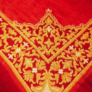 A close-up shows the corner of a vibrant red rug featuring a dense gold ornate foliate motif.