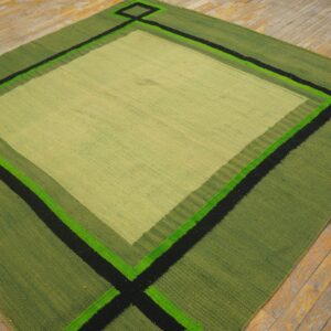 Geometric flatweave rug in green shades with black and neon accents on distressed wood flooring.