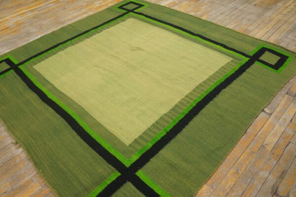Geometric flatweave rug in green shades with black and neon accents on distressed wood flooring.