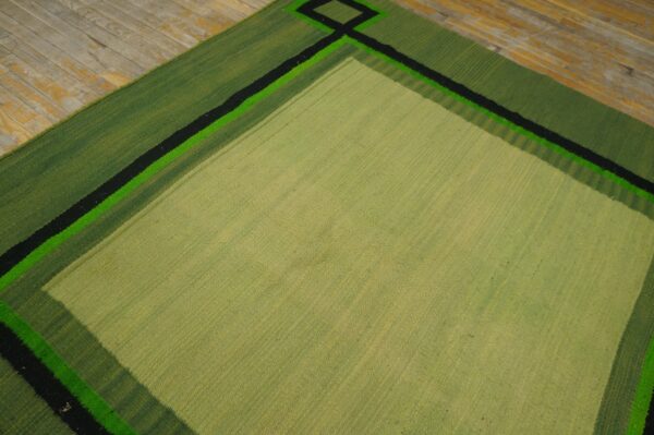 Geometric light and dark green flatweave rug with sharp black stripes shown on distressed plank flooring.