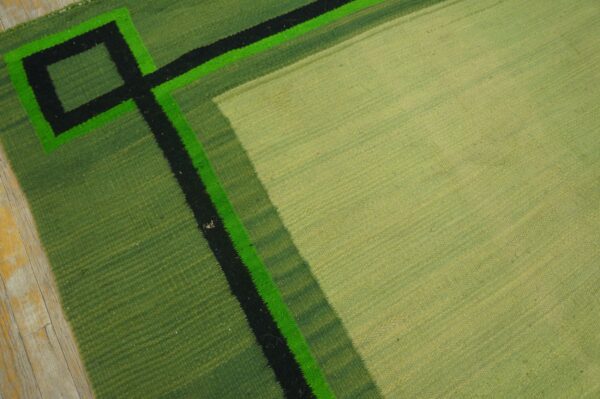 Pale green flatweave rug featuring geometric borders in darker greens, black, and bright neon green.