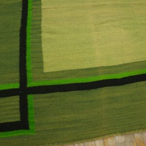 Geometric flatweave rug in shades of green, black, and neon green rests on light wood planks.