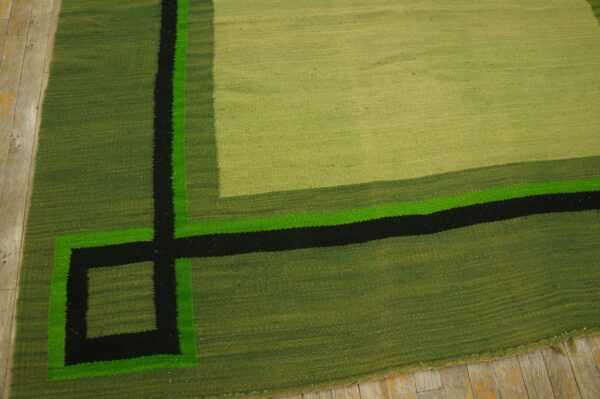 Geometric flatweave rug in shades of green, black, and neon green rests on light wood planks.