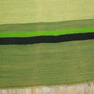 Flatweave rug with green, bright green, and black horizontal stripes shown on distressed wood floor.