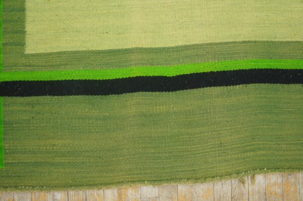 Flatweave rug with green, bright green, and black horizontal stripes shown on distressed wood floor.