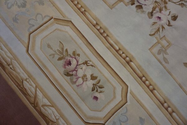 Low-pile cream and pale blue rug featuring pink floral motifs within light tan ornamental borders.