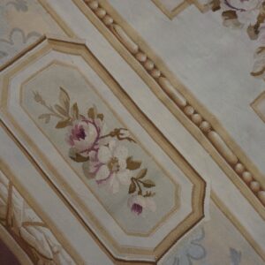 Low-pile rug detail showing pink and beige roses in a cartouche surrounded by striped architectural borders.