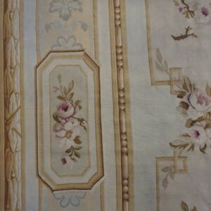 Pale gray-blue flatweave rug featuring soft pink and brown floral patterns and structured vertical borders on wood flooring.