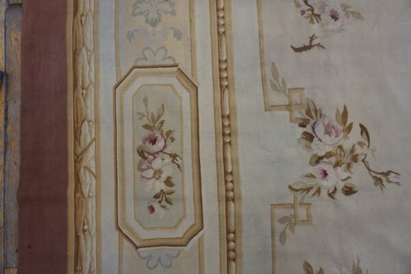 Pale gray-blue flatweave rug featuring soft pink and brown floral patterns and structured vertical borders on wood flooring.