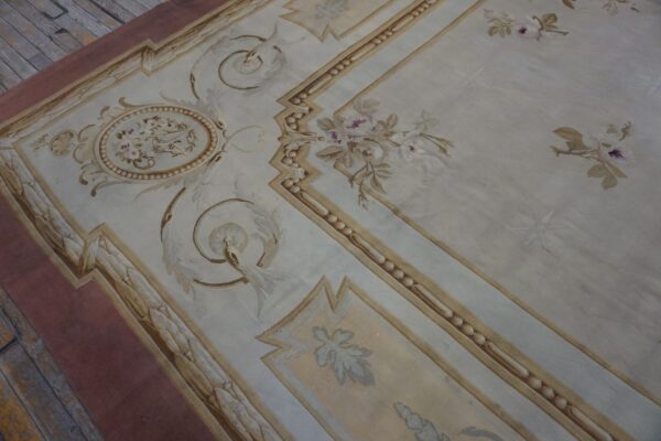Tightly woven rug in pale blue-grey and beige with scrolling floral cartouches rests on rustic wood floors.