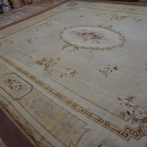 A large, pale beige rug with classical floral sprays and decorative tan borders is laid out on a wood floor.