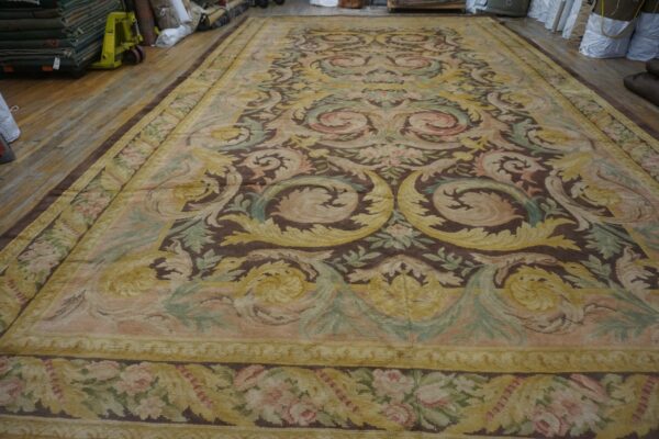 Low-pile tapestry rug with brown, yellow, pink, and sage scrollwork covering a wide-plank wood floor.