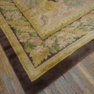 Floral border rug in pink, green, gold, and brown lays on textured, wide plank wood flooring.