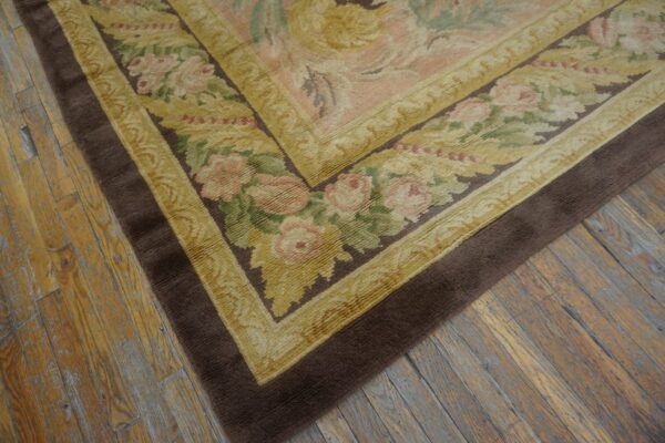 Floral border rug in pink, green, gold, and brown lays on textured, wide plank wood flooring.
