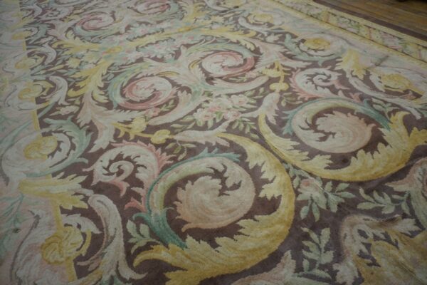 Ornate low-pile rug detailed with scrolling acanthus leaves in pale yellow, pink, and green on a brown background.