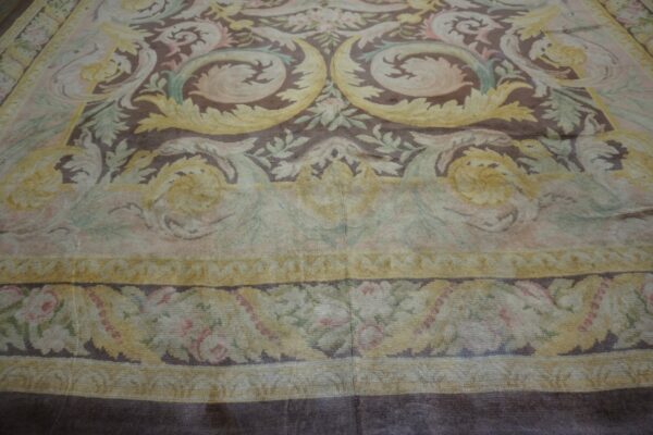 Large, ornate rug featuring brown, pale yellow, and muted green scrolling floral motifs and borders.