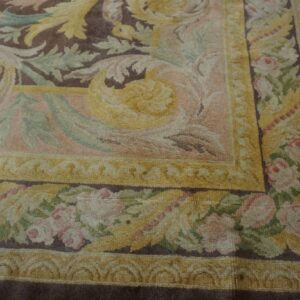High-pile rug corner showing a classic brown field, yellow scrollwork, and pink rose patterned borders.