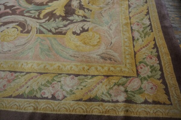High-pile rug corner showing a classic brown field, yellow scrollwork, and pink rose patterned borders.