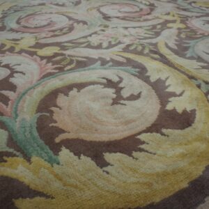 Brown rug with large scrolling acanthus leaves and flowers in shades of cream, pastel yellow, and green.