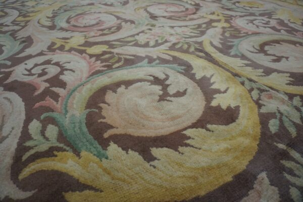 Brown rug with large scrolling acanthus leaves and flowers in shades of cream, pastel yellow, and green.