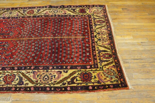 Red rug displaying vertical floral sprays and a wide yellow border on distressed wood floors.