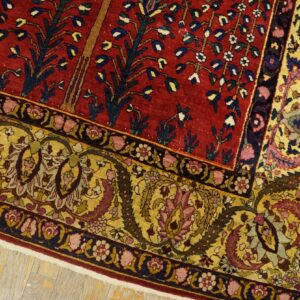 Red patterned rug featuring tree motifs and wide yellow floral borders on pale wooden plank flooring.