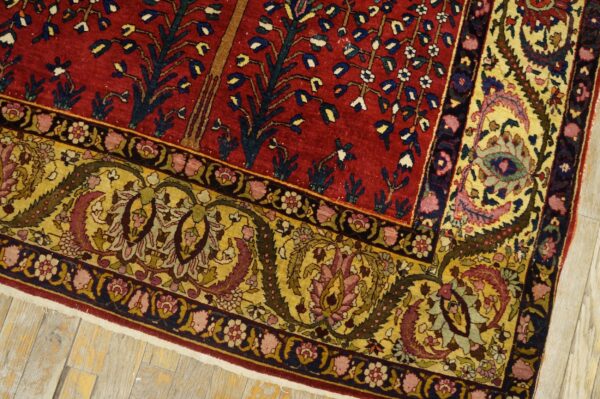 Red patterned rug featuring tree motifs and wide yellow floral borders on pale wooden plank flooring.