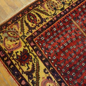 A traditional rug with a red floral field and a wide yellow border rests on rustic wood planks.