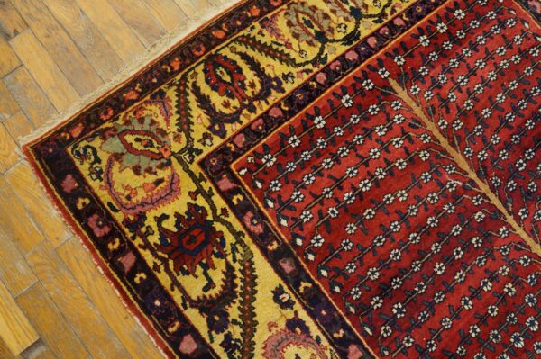 A traditional rug with a red floral field and a wide yellow border rests on rustic wood planks.