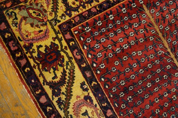 Traditional rug detail showing a deep red field with vine pattern and a wide yellow border resting on wood flooring.