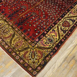 Ornate red field rug with a detailed gold and yellow floral border rests on light wood planks.
