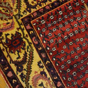 Red field rug with stylized white flowers, contrasting a golden yellow patterned border on wood.