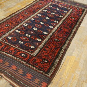 Low-pile red and blue rug with floral and geometric patterns sits diagonally on light, worn wood floors.
