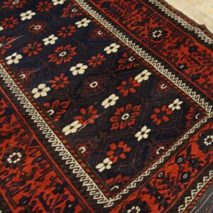 Close-up of a dark blue and red patterned rug with cream accents lying on light wooden floorboards.