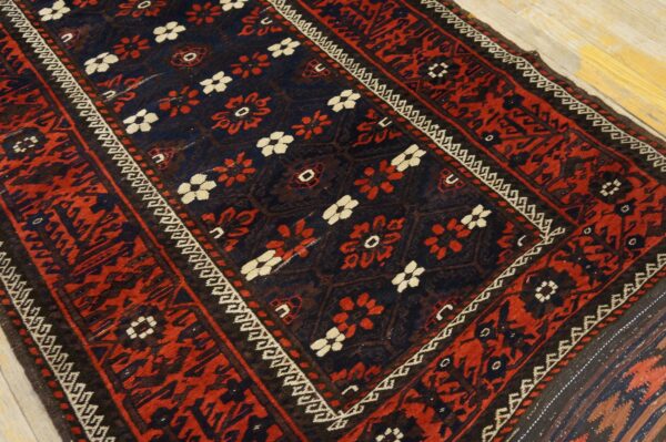 Close-up of a dark blue and red patterned rug with cream accents lying on light wooden floorboards.