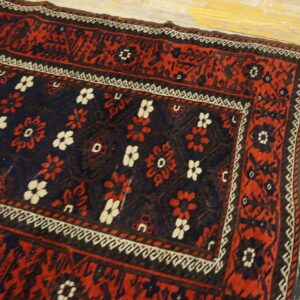 Traditional red and navy rug with white floral patterns and geometric borders resting on light distressed wood floors.