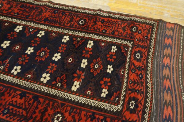 Traditional red and navy rug with white floral patterns and geometric borders resting on light distressed wood floors.