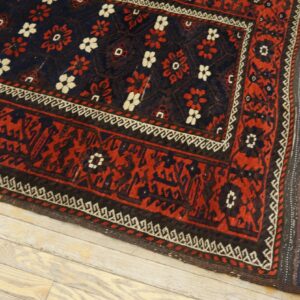 Low-pile rug in navy and red with white flower motifs and complex borders rests on whitewashed wood planks.
